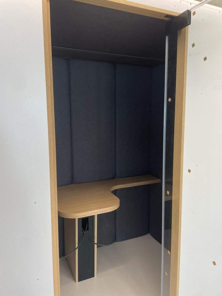 Interior of a single acoustic booth with a corner wood desk and upholstered panels