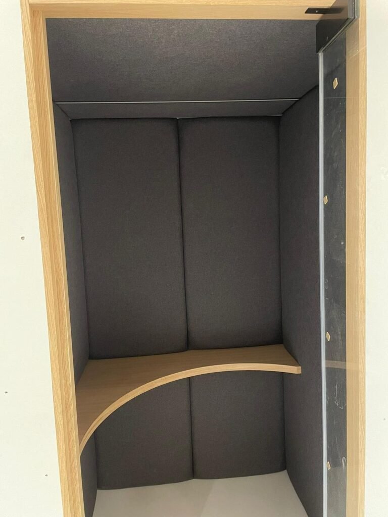 Interior of an acoustic booth with a curved wood shelf and upholstered acoustic panels