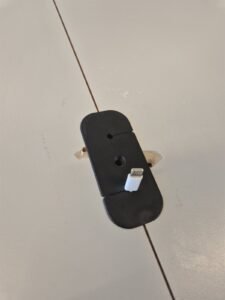 Soporte negro impreso en 3D para cable USB, fijado sobre la junta entre dos tableros.