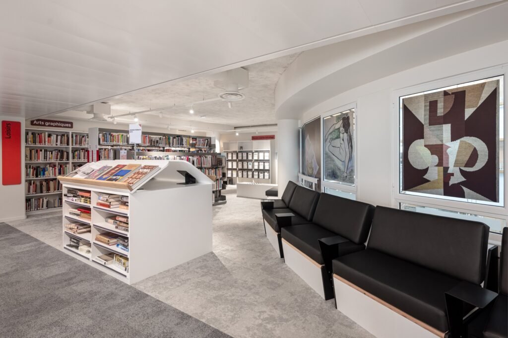 Black upholstered lounge benches and a white book display unit beside framed artworks at the BPI Lumière